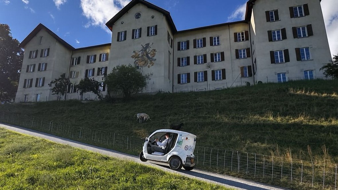 Weisses eMiMo-Fahrzeug fährt auf der Strasse am Kloster Löwenberg in Schluein.